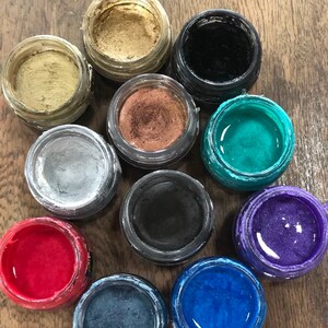 May include: Ten small round jars of metallic paint in various colours, including gold, silver, black, red, blue, green, and purple.