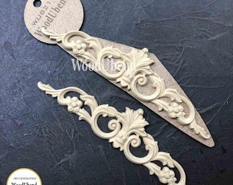 May include: Two cream-colored, ornate wood appliques with floral and scroll designs. One is mounted on a tan, triangular piece. A circular tag with the text "WoodUbend" is visible. The appliques are on a dark gray surface.