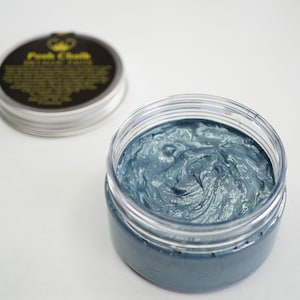 May include: A small jar of teal blue metallic paint with a black lid. The lid has a gold crown and the words "Folk Chalk" written on it.
