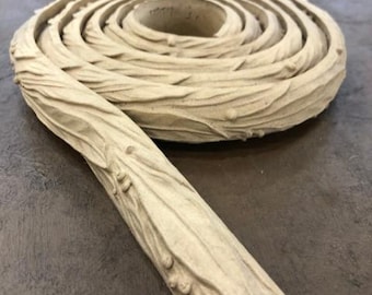 May include: A light beige, carved wood trim piece, coiled in a spiral. The trim has a textured, organic design with a branch-like appearance. The piece is likely for home decor or woodworking projects.