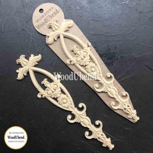 May include: Two decorative wood appliques with floral and scroll designs. One applique is attached to a cardboard tag with the text "WUB2096 WoodUbend". The appliques are cream-colored and feature intricate details, perfect for craft projects.