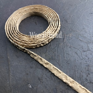 May include: A beige, textured, decorative trim with a repeating pattern. The trim is rolled up in a coil.