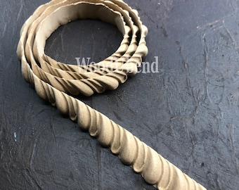 Puede incluir: Una moldura decorativa de color beige claro, con un diseño en espiral repetitivo. La moldura está enrollada en espiral y descansa sobre una superficie oscura y texturizada. El texto "Wood Trend" es visible en la superficie.