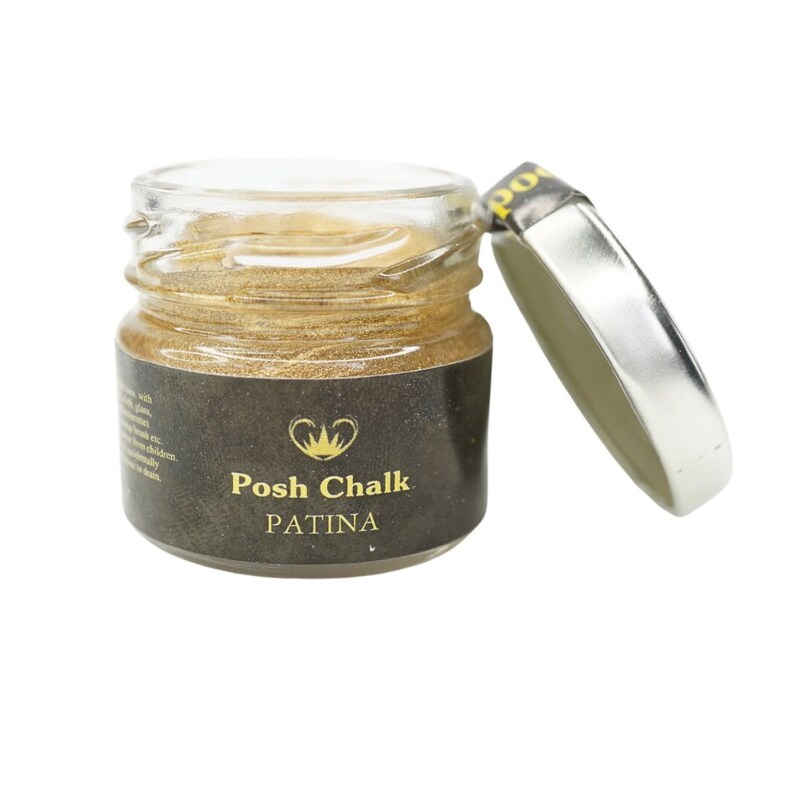May include: A small glass jar with a silver lid containing gold metallic paint. The jar has a black label with the text "Posh Chalk PATINA" in gold lettering.