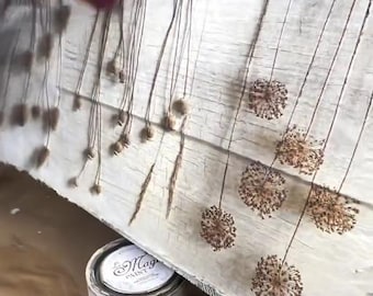 May include: A white wooden sign with brown dried flowers and a white paint can labeled "Magic Paint" with a 500 ml capacity. The sign is being painted with a white paint brush.