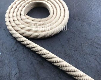 May include: A close-up of a thick, rope-like wooden trim with a braided design. The trim is light beige in color and is coiled up on a dark gray surface.