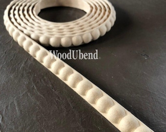 Puede incluir: Un rollo de moldura de madera sin terminar con un diseño de bolas repetidas. La moldura es de color beige y tiene el texto "WoodUbend" impreso. La moldura está sobre una superficie gris oscuro.