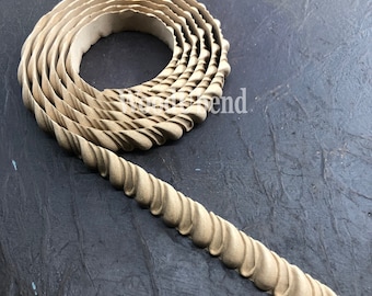 Puede incluir: Un adorno decorativo beige enrollado, con un diseño texturizado en forma de cuerda. El adorno está hecho de un material flexible y se muestra sobre un fondo oscuro y texturizado. El adorno probablemente se utiliza para manualidades o decoración.