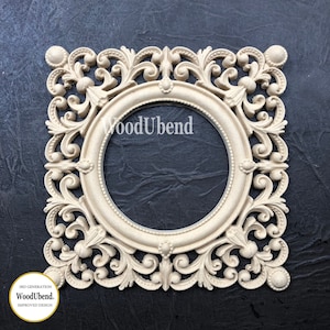 May include: A white, ornate, square-shaped frame with a circular opening in the center. The frame has a decorative, floral design and the text "WoodUbend" is visible in the center.