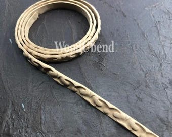 May include: A beige leather cord with a decorative pattern. The cord is coiled and has a textured surface.
