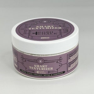 Pode incluir: Um frasco branco com um rótulo roxo com o texto "SMART TEXTURIZER" e "POSH CHALK". O frasco contém 200 ml de produto e foi concebido para madeira, vidro, cerâmica, metal e laminado.