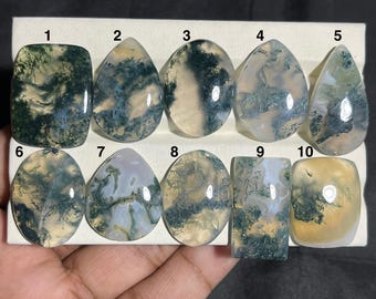May include: Ten polished moss agate gemstones of various shapes, including rectangular, oval, and teardrop. The stones display a mix of green, white, and translucent colors, with unique patterns resembling moss or landscapes. Each stone is numbered for identification.