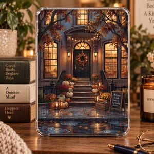 May include: A clear tablet case featuring an illustration of a house entrance with a wreath on the door, pumpkins, and potted flowers on the steps. A small chalkboard sign reads Autumn & Ink, Come In, It's Reading Season. Rain falls on the wet pavement.