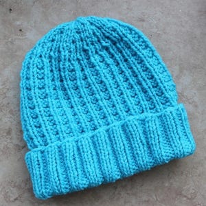 Può includere: Un berretto lavorato a maglia turchese con bordo a coste e motivo a punto strutturato. Il cappello è realizzato in filato morbido ed è progettato per tenere la testa al caldo. Il cappello è di colore pieno ed è adatto al clima freddo.