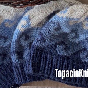 May include: Close-up of three knitted beanies in shades of blue and grey. The beanies feature a textured pattern and the text "TopacioKnits" in white.