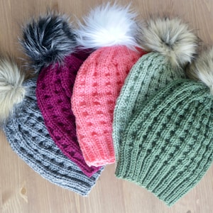May include: Four knitted winter hats with faux fur pom poms in gray, burgundy, pink, and green.