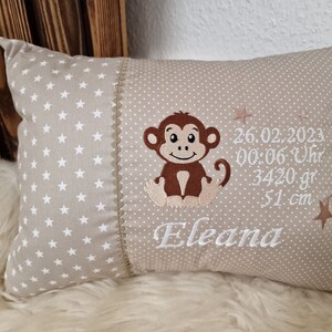 Könnte beinhalten: Ein beiges Kissen mit weißen Sternen auf der einen Seite und einem braunen Affen, dem Datum 26.02.2023, 00:06 Uhr, 3420 g, 51 cm, und dem Namen Eleana auf der anderen Seite.