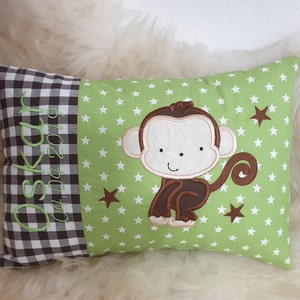 Könnte beinhalten: Ein grünes Kissen mit weißen Sternen und einem braunen Affen, der darauf gestickt ist. Das Kissen hat einen braunen und weißen karierten Rand mit dem Namen "Oskar" und dem Datum "04.04.2019", das darauf gestickt ist.