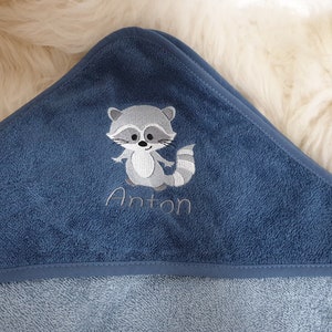 以下が含まれることがあります： アントンという名前が刺繍された、アライグマの刺繍が施された青いフード付きタオルです。