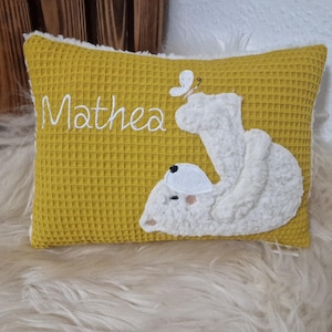 Könnte beinhalten: Ein gelbes Waffel-Kissen mit weißer Stickerei, auf dem "Mathea" steht, und einem weißen Plüschbären mit einem Schmetterling auf dem Rücken.