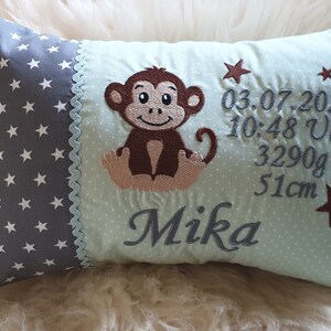 Könnte beinhalten: Ein hellblaues und graues Kissen mit einem braunen Affen und Sternen bestickt. Das Kissen hat auch den Text "03.07.2021 10:48 Uhr 3290g 51cm Mika" bestickt.