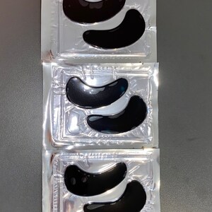 May include: Three individual packages of black under-eye patches. Each package contains two crescent-shaped patches.