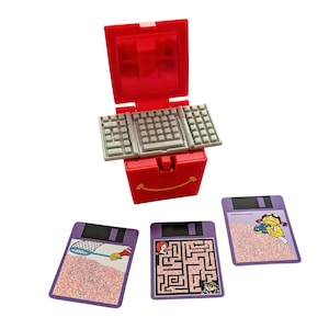 May include: A red plastic toy box with a keyboard lid and three game cards. The cards feature a maze, a net, and a character with a net.