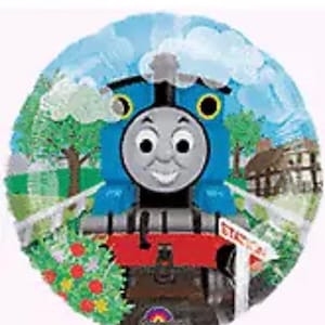 May include: A blue and red Thomas the Tank Engine balloon with a smiling face. The balloon is surrounded by green foliage and a blue sky with white clouds.
