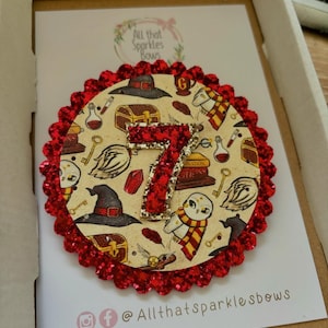 K&ouml;nnte beinhalten: Ein roter Glitzerkreis mit einem wei&szlig;en und goldenen Harry-Potter-Design mit der Zahl 7, Eulen und einem Hut. Der Text "All that sparkles bows" befindet sich auf dem wei&szlig;en Hintergrund.