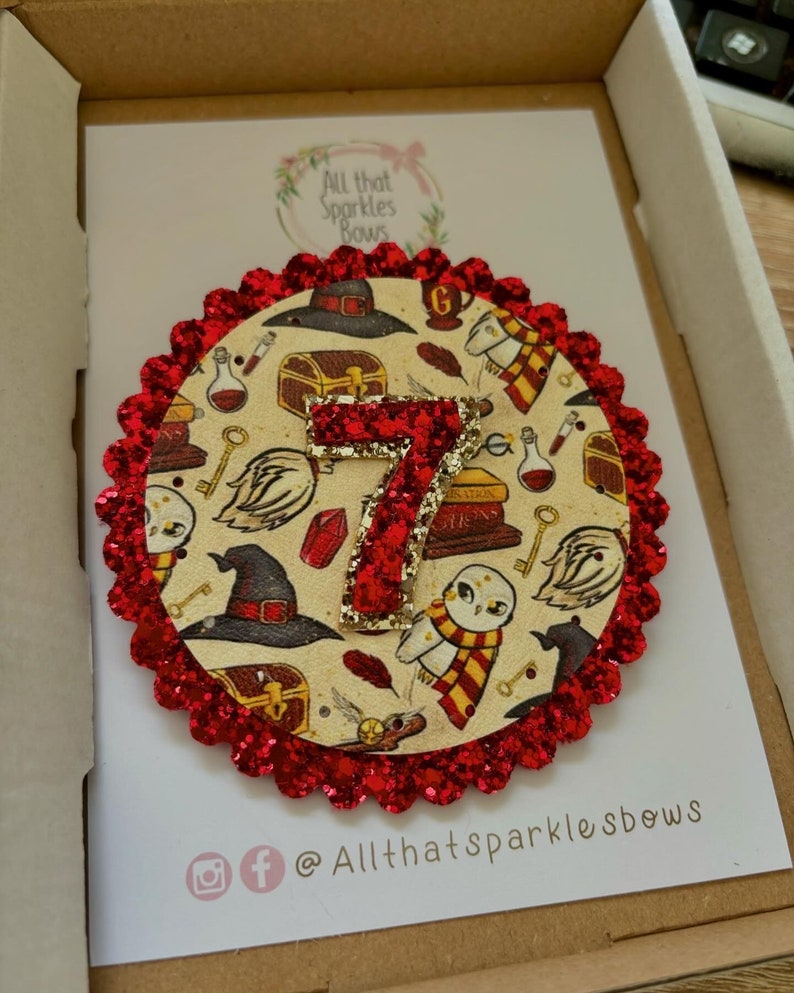 K&ouml;nnte beinhalten: Ein roter Glitzerkreis mit einem wei&szlig;en und goldenen Harry-Potter-Design mit der Zahl 7, Eulen und einem Hut. Der Text "All that sparkles bows" befindet sich auf dem wei&szlig;en Hintergrund.