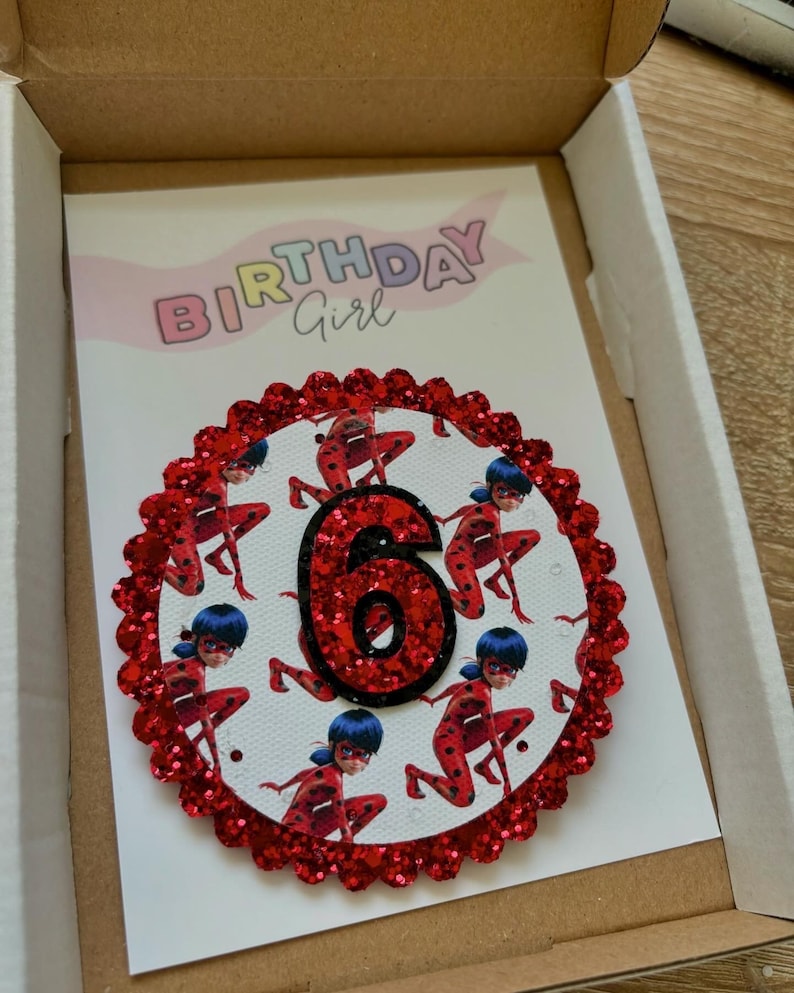 K&ouml;nnte beinhalten: Rote Glitzer-Geburtstagskarte mit einem roten und schwarzen Marienk&auml;fer-Design und der Zahl 6 in der Mitte. Die Karte tr&auml;gt oben den Schriftzug "Birthday Girl".