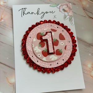 May include: A white card with the text "Thankyou" and a red glitter circle with a pink circle inside. The pink circle has a white number "1" and a strawberry pattern.