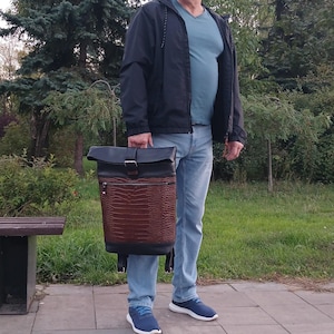 Pode incluir: Uma mochila roll-top com uma sec&ccedil;&atilde;o superior em pele preta e uma sec&ccedil;&atilde;o inferior em pele castanha com um padr&atilde;o texturado de pele de crocodilo. O saco inclui um bolso frontal com fecho, um fecho de fivela met&aacute;lica e al&ccedil;as pretas ajust&aacute;veis.