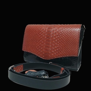 May include: A brown and black leather crossbody bag with a snakeskin pattern on the flap. The bag has a black strap and silver hardware. The bag is set against a black background.