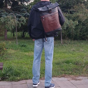 Pode incluir: Uma mochila roll-top com uma sec&ccedil;&atilde;o superior preta e uma sec&ccedil;&atilde;o inferior castanha com um padr&atilde;o texturizado de pele de crocodilo. O saco inclui um bolso frontal com fecho, um fecho de fivela met&aacute;lica e al&ccedil;as pretas ajust&aacute;veis.