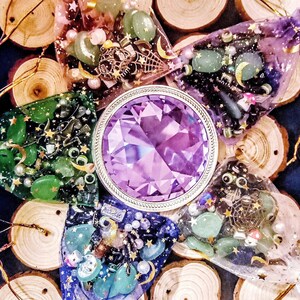 May include: Assortment of small, colorful, and sparkly bags filled with beads and charms, arranged on wooden rounds with a purple crystal in the center.