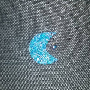 May include: A silver chain necklace with a blue glitter crescent moon pendant and a small blue bead charm.