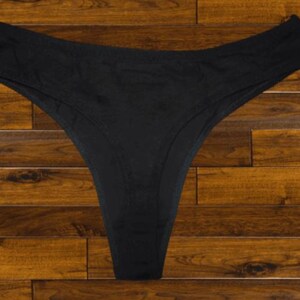 May include: Black lace thong underwear on a wooden background.