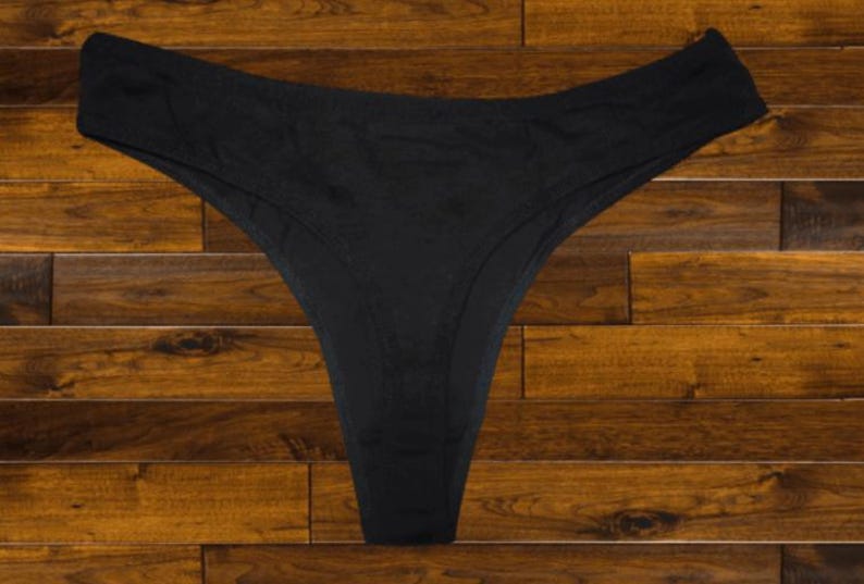 May include: Black lace thong underwear on a wooden background.