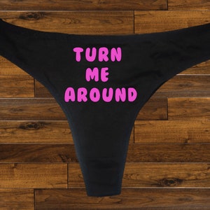 May include: Black lace underwear with the text "TURN ME AROUND" printed in pink.