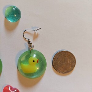 May include: A pair of green and yellow earrings with a small yellow rubber ducky inside a clear green resin circle. The earrings are hanging from silver hooks.