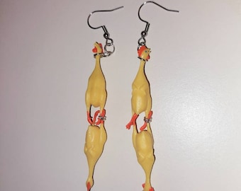 May include: A pair of novelty earrings featuring two yellow rubber chicken figures per earring. The chickens have red feet and combs, and are connected by silver-colored rings. The earrings hang from silver-colored fish hook ear wires.