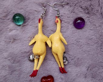 Könnte beinhalten: Ein Paar gelbe Gummiküken-Ohrringe mit roten Füßen und einem kleinen Eihänger an jedem Küken. Die Ohrringe hängen an silbernen Haken.
