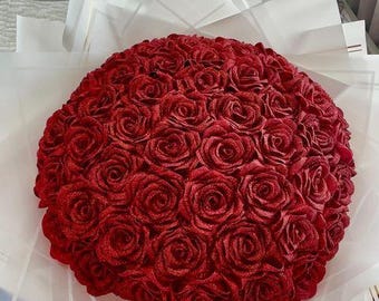 Può includere: Un grande bouquet di rose di velluto rosso disposte in forma circolare. Le rose sono circondate da carta velina bianca.