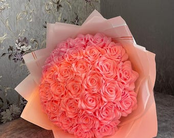 May include: A bouquet of pink foam roses arranged in a white paper wrapping. The roses are arranged in a circular shape and are illuminated from below.