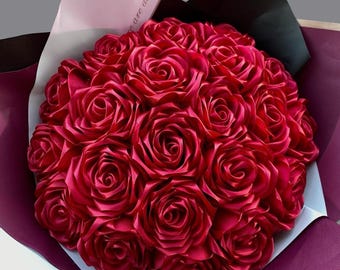 Könnte beinhalten: Ein Strauß aus 20 tief roten Satinrosen, die in einer kreisförmigen Form angeordnet sind. Die Rosen sind in weißes und burgunderfarbenes Papier mit einem schwarzen Band eingewickelt.