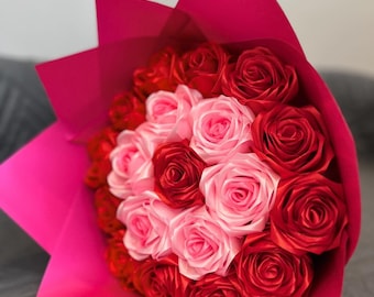 Könnte beinhalten: Ein Strauß aus rosa und roten Satinrosen, verpackt in pinkfarbenem Papier.
