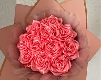 May include: A bouquet of pink satin roses wrapped in a peach-colored paper with a gold trim.
