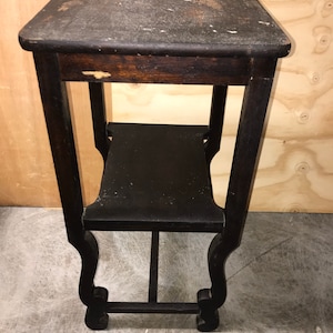 May include: A dark brown wooden side table with two shelves and decorative legs. The table has a distressed finish and is in good condition.