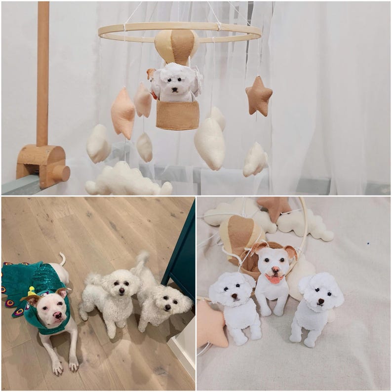 May include: A wooden mobile with a white, brown, and beige color scheme. The mobile features a hot air balloon with a white dog inside, clouds, and stars. There are three white dogs on the floor below the mobile.
